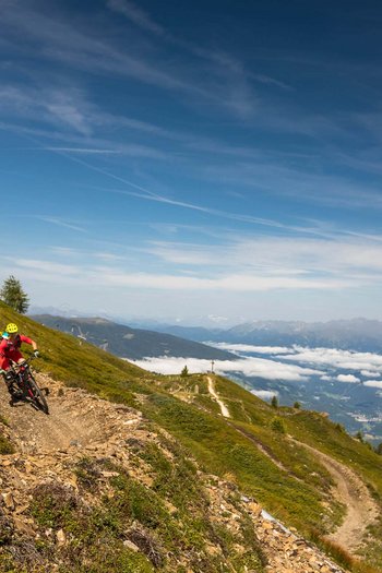 Bike offers and impressions Two mountain bikers riding a trail on a mountainside with panoramic valley and mountain views