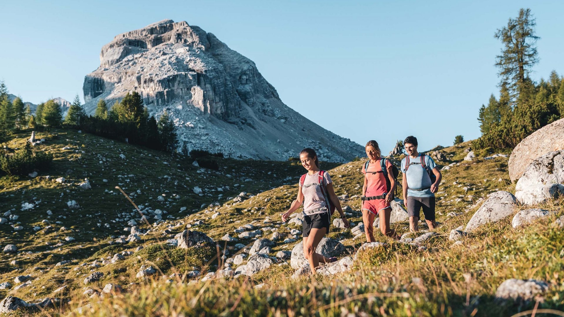 Wandern und Wellness: Ihr Aktivhotel in Südtirol Drei Wanderer mit Rucksäcken auf Bergpfad bei sonnigem Wetter