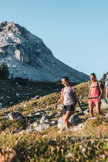 Excelsior: Wanderhotel in den Dolomiten Drei Wanderer mit Rucksäcken auf Bergpfad bei sonnigem Wetter