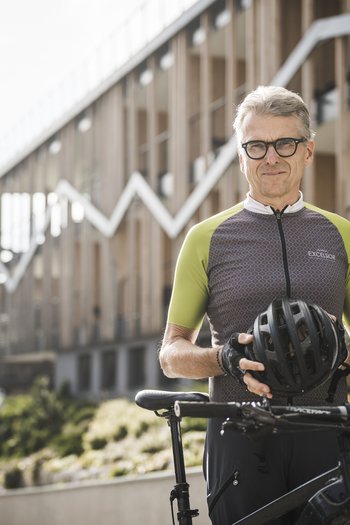 Excelsior: Wanderhotel in den Dolomiten Älterer Mann mit Fahrradhelm neben Fahrrad in urbanem Umfeld