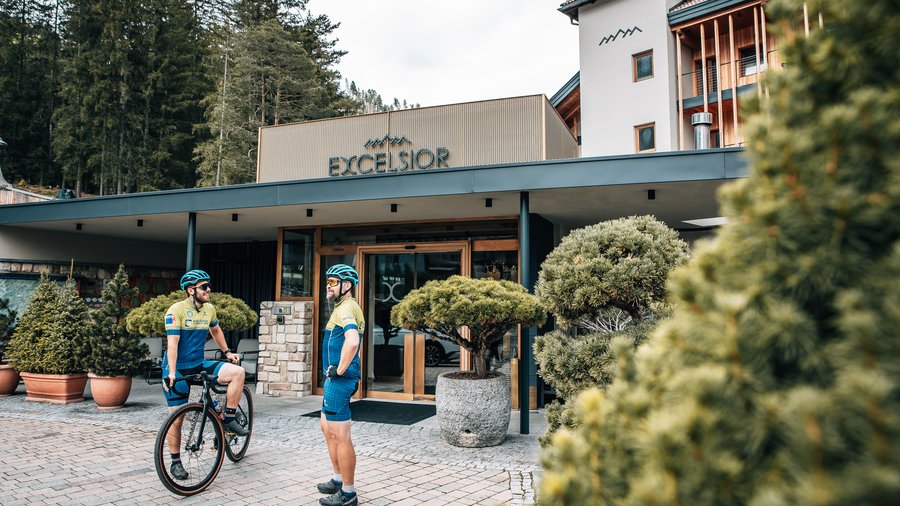 Bike-Kompetenz Zwei Radfahrer in Sportkleidung vor Hotel Excelsior mit Bäumen