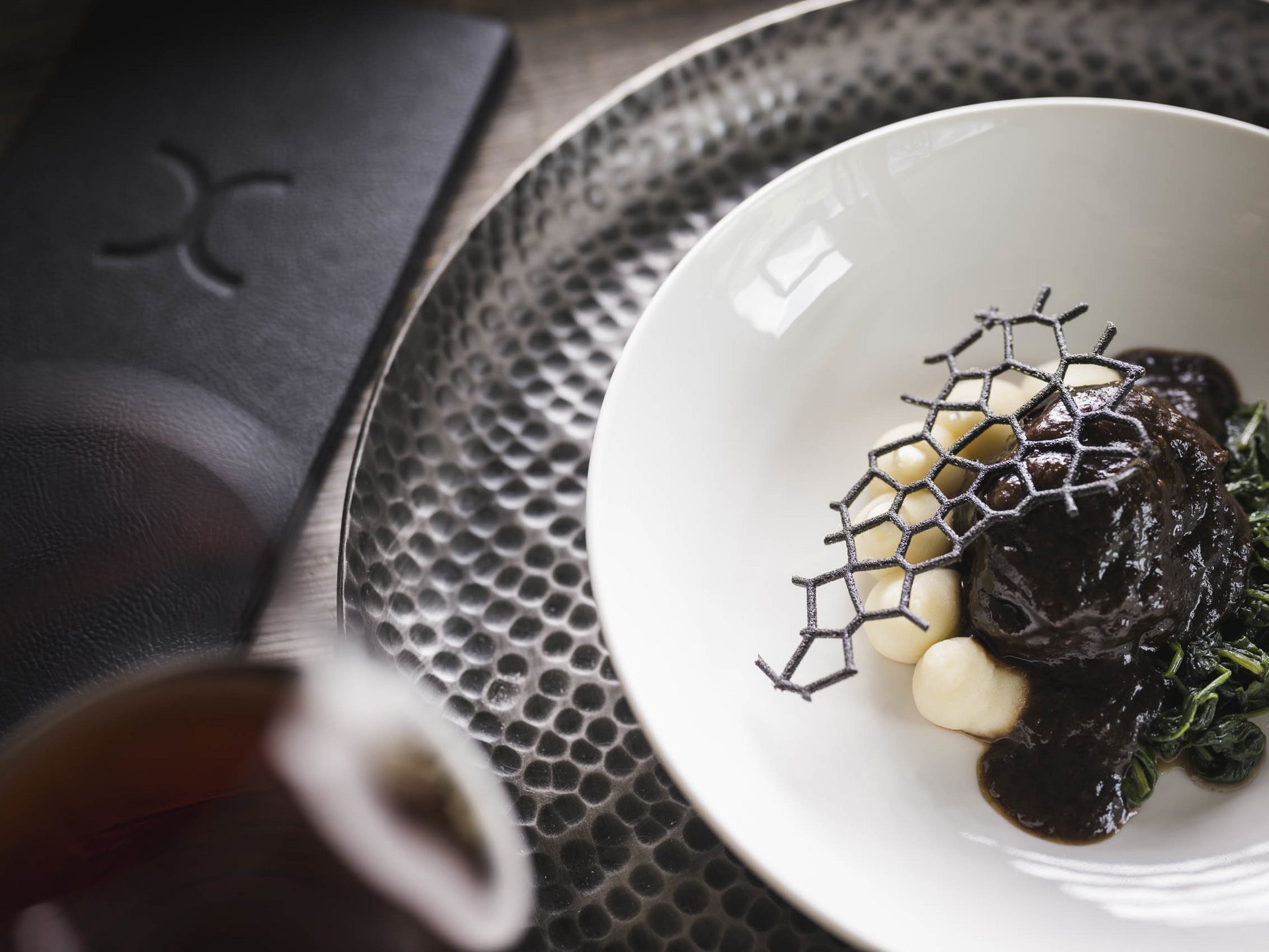 Hotel per celiaci Piatto gourmet con salsa scura, spinaci e gnocchi su piatto bianco