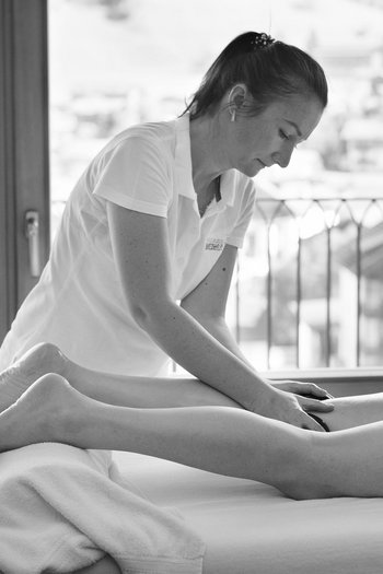 Benvenuti nel vostro hotel al Plan de Corones! Donna che fa un massaggio con pietre calde a una persona distesa in una stanza luminosa