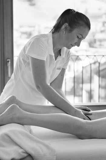 Ihr Hotel in St. Vigil in Enneberg! Frau gibt einer liegenden Person eine Hot-Stone-Massage in einem hellen Raum