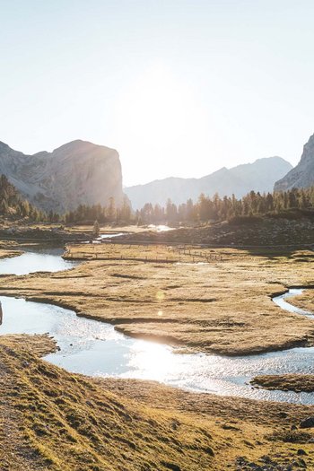 Excelsior: Wanderhotel in den Dolomiten Drei Wanderer gehen an einem Fluss in einer sonnigen Berglandschaft