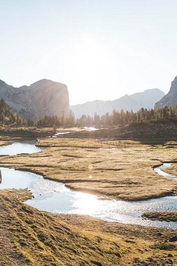 Wanderhotels Südtirol in the Dolomites Three hikers walking along a river in a sunny mountain landscape