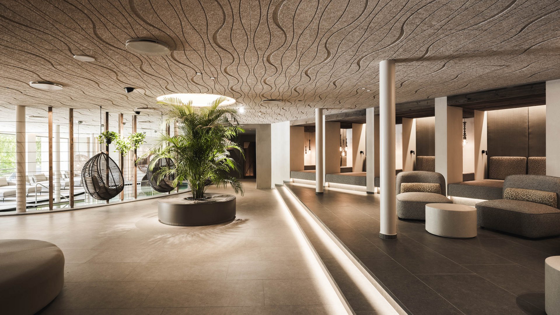 Hotel con infinity pool in Alto Adige: l’Excelsior Interno moderno con aree salotto, piante e sedie a dondolo appese