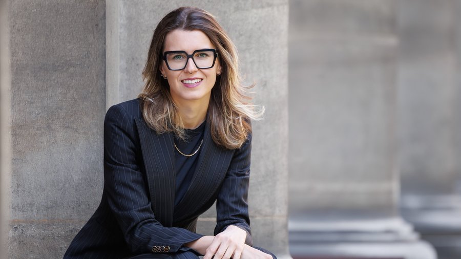 Dolomiten-Hotel für Bergmenschen Frau im schwarzen Anzug und Brille sitzt vor einer Gebäudefassade