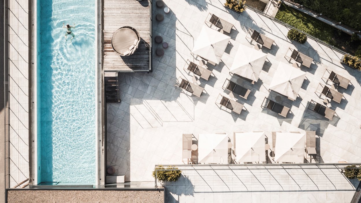 #myexcelsior Sunday News 09.02.2025 Vista dall'alto di una piscina con persona e terrazza adiacente con lettini e ombrelloni