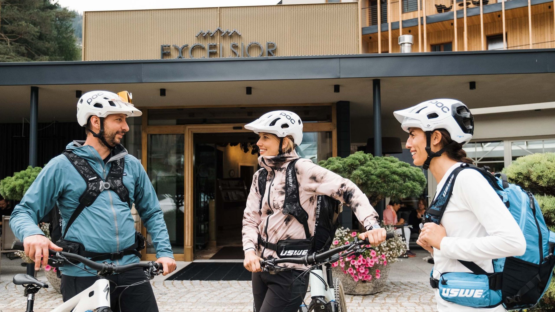 Bike-Kompetenz Drei Radfahrer mit Helmen vor dem Hotel Excelsior im Gespräch