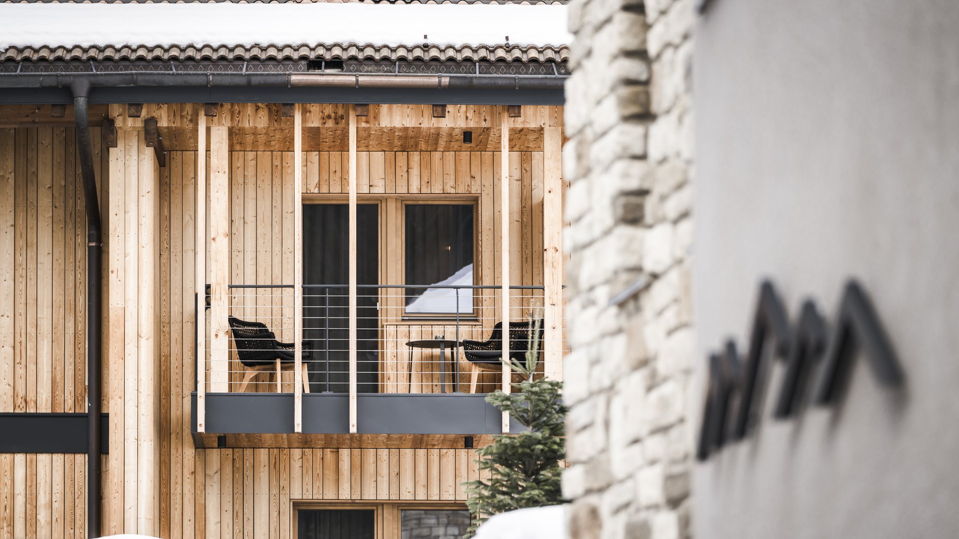 Hotel di lusso in Alto Adige: i nostri ospiti Balcone con due sedie nere su casa in legno chiaro con neve