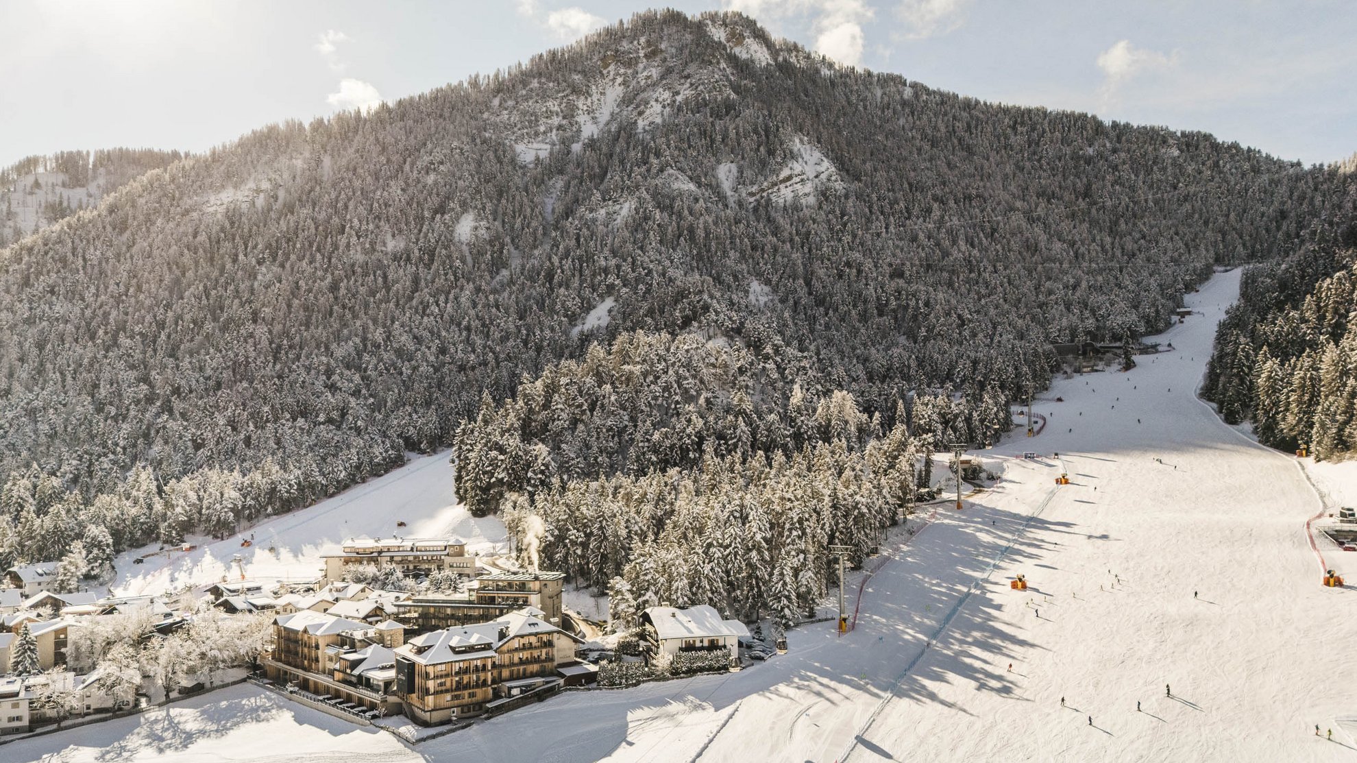 Hotel con centro spa a San Vigilio di Marebbe Comprensorio sciistico innevato con piste, impianti di risalita e hotel ai piedi di una montagna boscosa