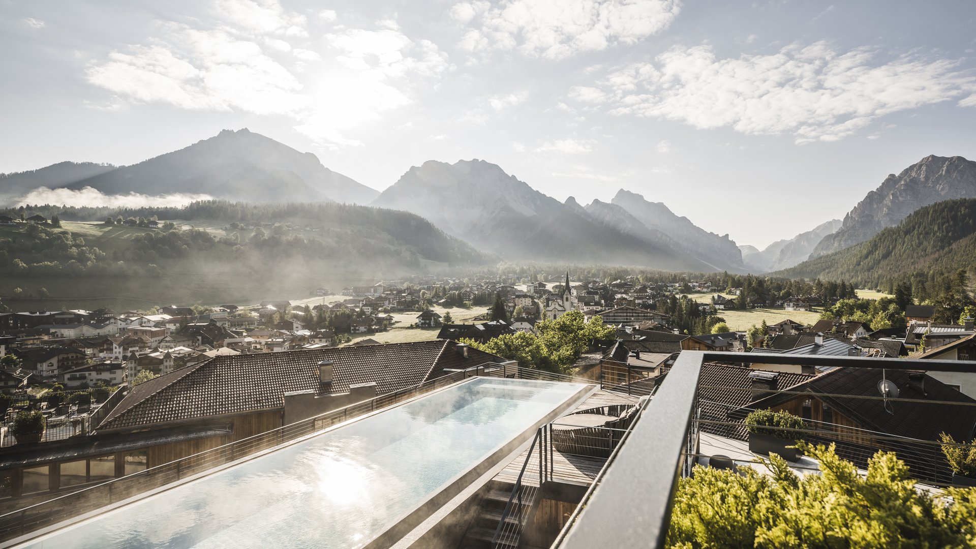 Ihr Hotel in St. Vigil in Enneberg! Infinity-Pool mit Blick auf eine Berglandschaft und Stadt im Tal