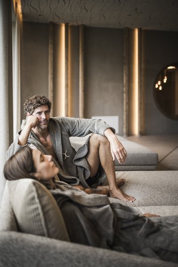 Hotel in den Dolomiten für adults only Mann und Frau entspannen in Bademänteln auf einer Couch in modernem Raum