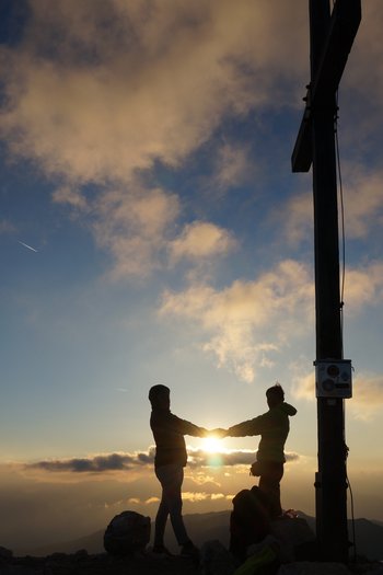 San Vigilio di Marebbe: escursioni per famiglie Due persone si tengono per mano vicino a una croce di vetta al tramonto