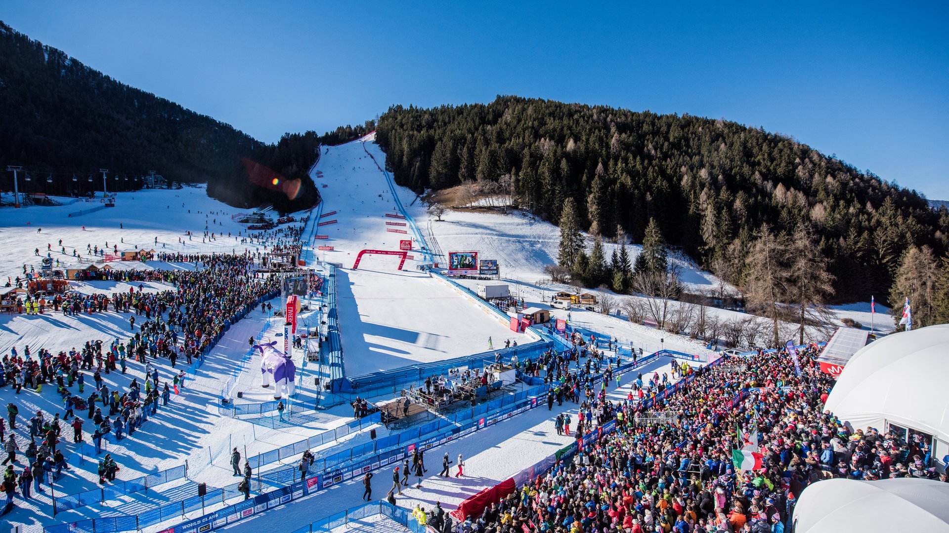 Around the hotel on the slopes in South Tyrol Crowd at ski race on snowy slope with forested mountain in background