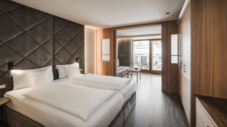 Wohnen am Kronplatz: Hotel an der Piste Modernes Hotelzimmer mit Doppelbett und Blick auf Balkon und Außenbereich