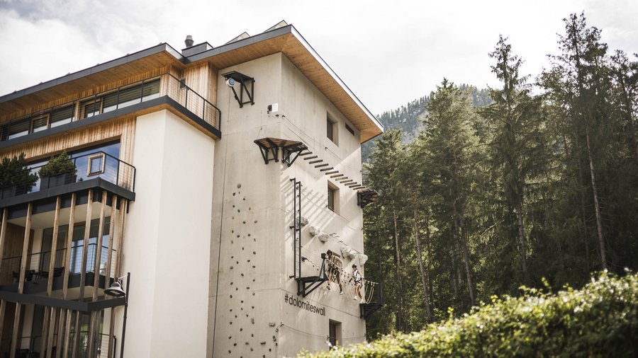 Wellnesshotel in den Dolomiten Kletterwand an einem modernen Gebäude mit zwei Kletterern in einem Waldgebiet