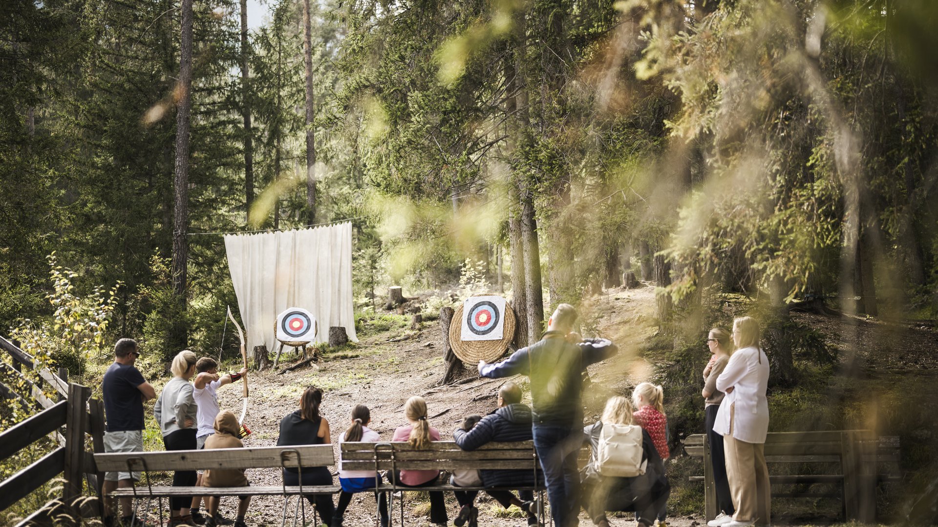 Mountain hotel in the Dolomites/South Tyrol Children and adults practicing archery in the forest in front of two targets