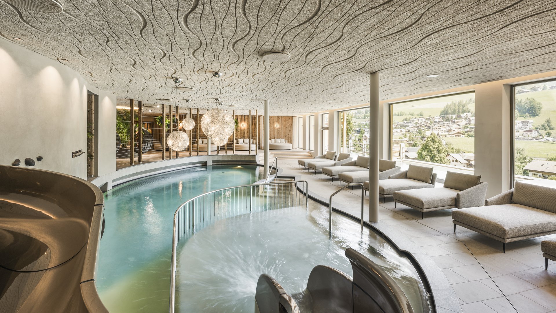 Wellnesshotel in den Dolomiten Moderner Innenpool mit Liegen und Panoramafenstern mit Bergblick