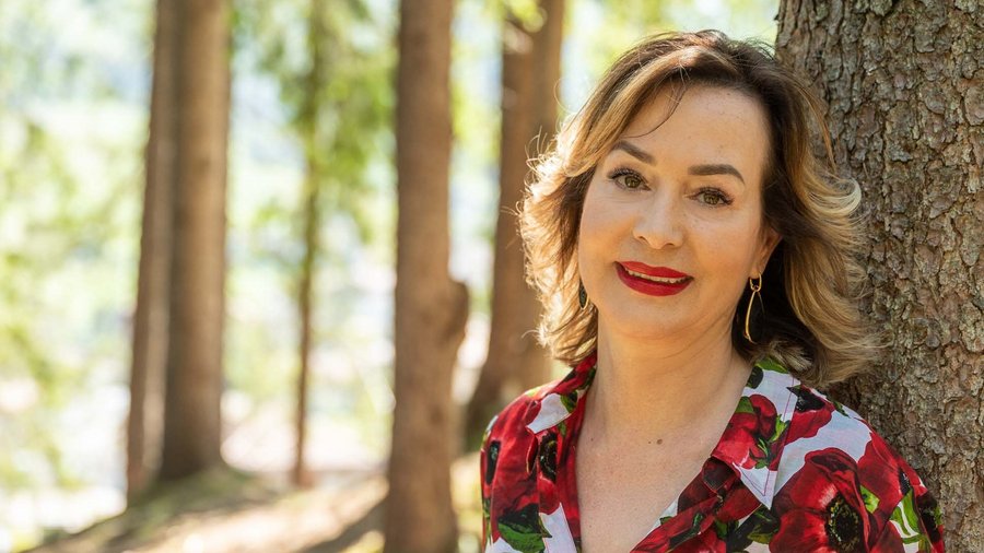 Dolomiten-Hotel für Bergmenschen Frau mit rotem Blumenhemd lehnt an Baum im sonnigen Wald