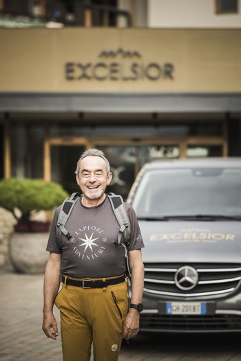 Excelsior: Wanderhotel in den Dolomiten Lächelnder Mann mit Rucksack vor Excelsior-Hotel und Mercedes-Fahrzeug