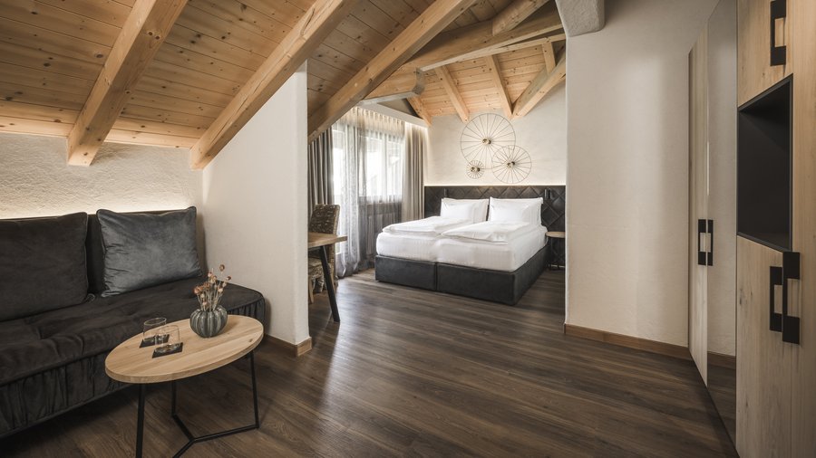 Wohnen am Kronplatz: Hotel an der Piste Gemütliches Hotelzimmer mit Holzbalken, Bett und Sitzbereich