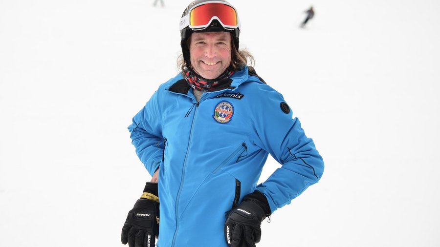 Hotel at Plan de Corones/Kronplatz on the slopes Man in blue ski jacket and helmet smiling on snowy slope