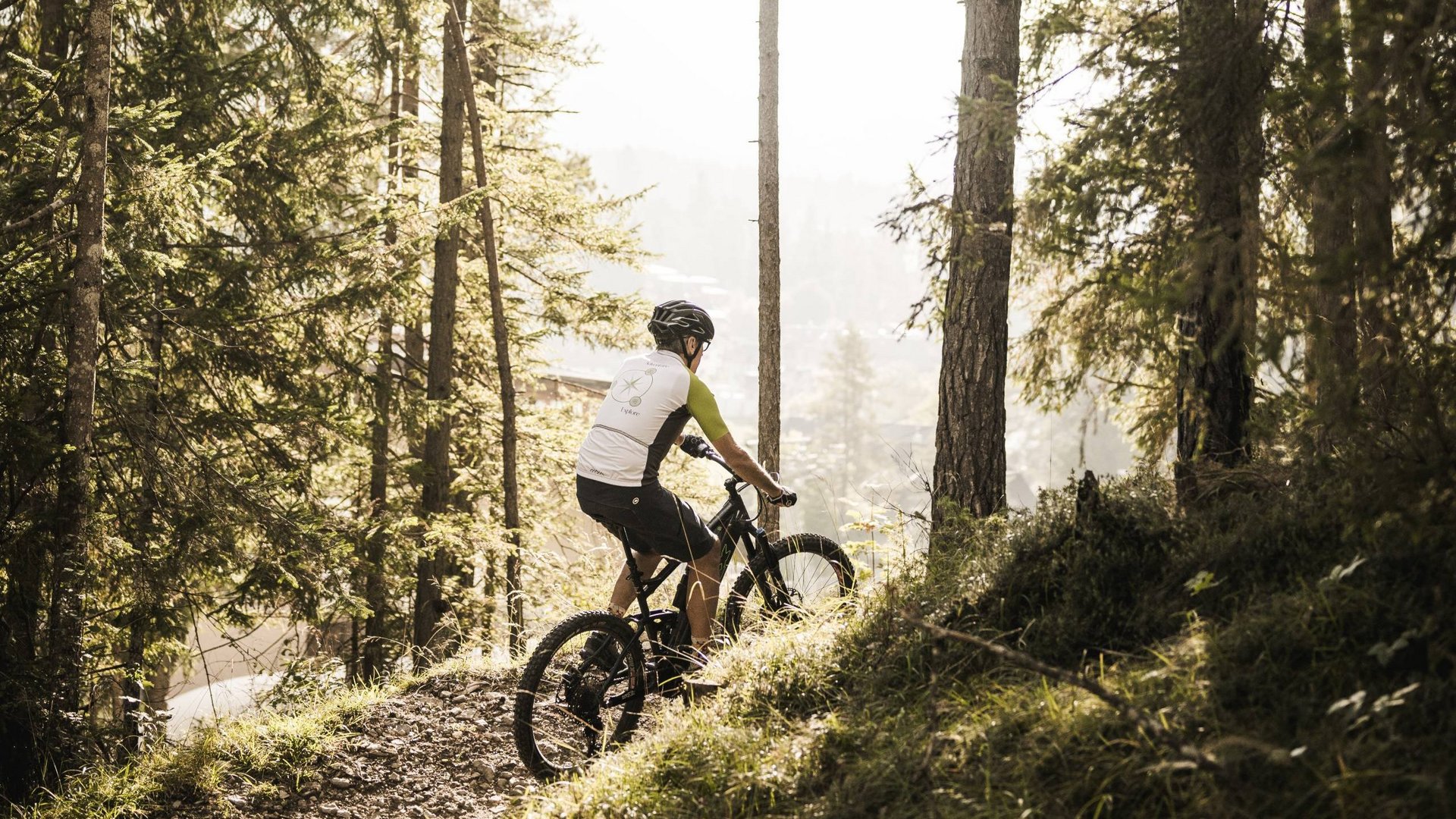 Eines der Bike-Hotels in Südtirol Mountainbiker fährt durch bewaldeten Weg im Sonnenlicht