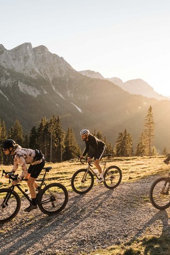 Eines der Bike-Hotels in Südtirol Drei Radfahrer fahren auf einem Bergweg bei Sonnenuntergang mit Bergen im Hintergrund