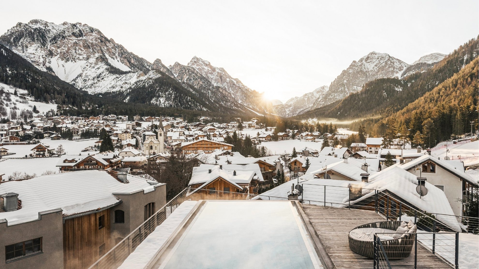 Angebote: Wellness und Wandern | Südtirol Blick auf verschneites Bergdorf mit Infinity-Pool und Sonnenuntergang