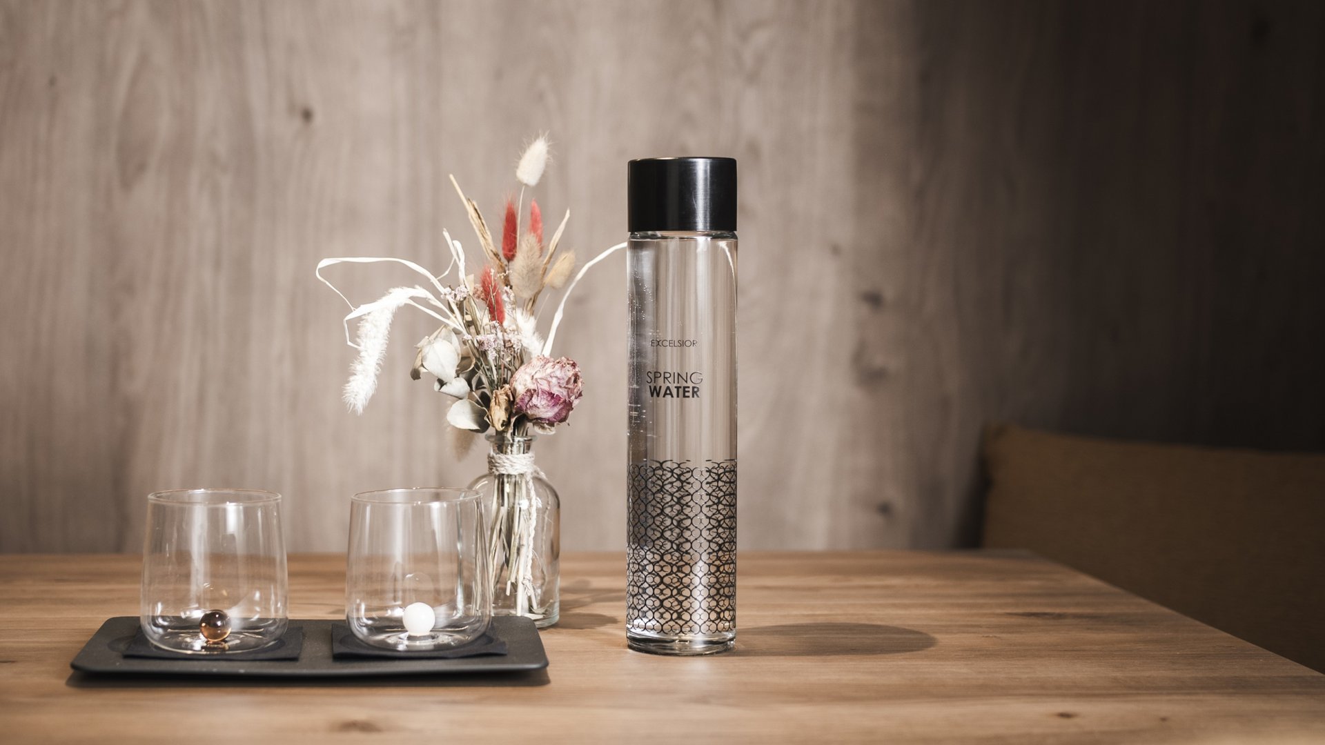 Sustainable hotels in South Tyrol? The Excelsior! Spring water bottle, two glasses and dried flowers on wooden table