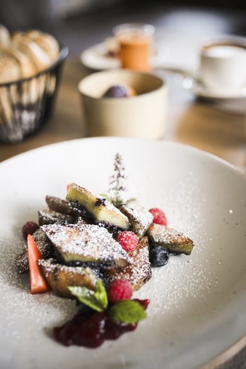 The gourmet hotel in South Tyrol Delicious dessert with powdered sugar, berries, and mint leaf on white plate