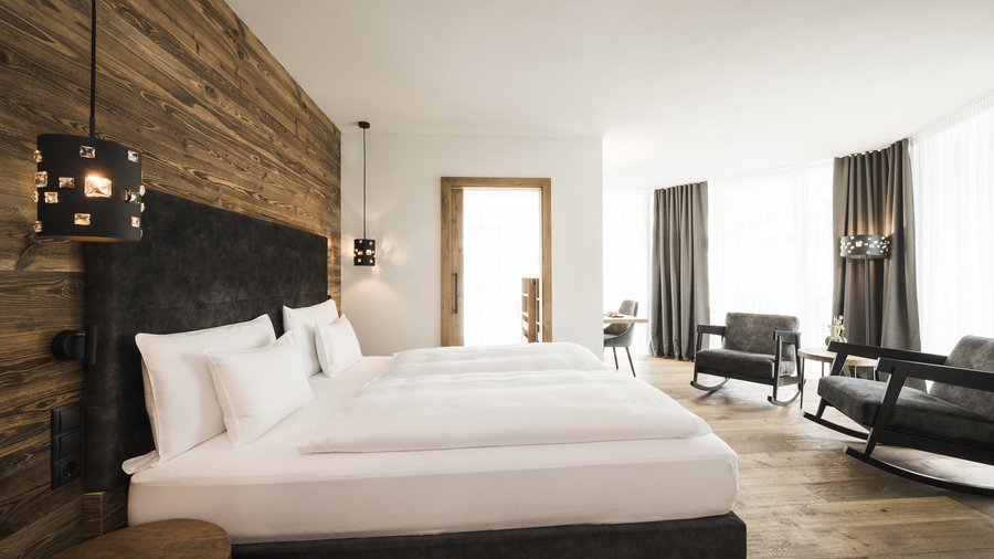 Wellness nel nostro hotel sulle Dolomiti: schiena al top Camera d'hotel moderna con parete di legno, letto matrimoniale e angolo con poltrone a dondolo