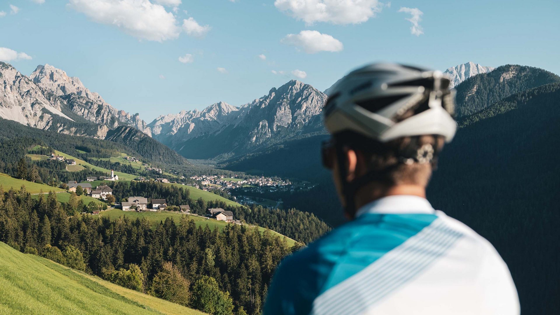 Bike-Verleih Radfahrer blickt auf ein Tal mit Bergen und Dörfern bei klarem Himmel
