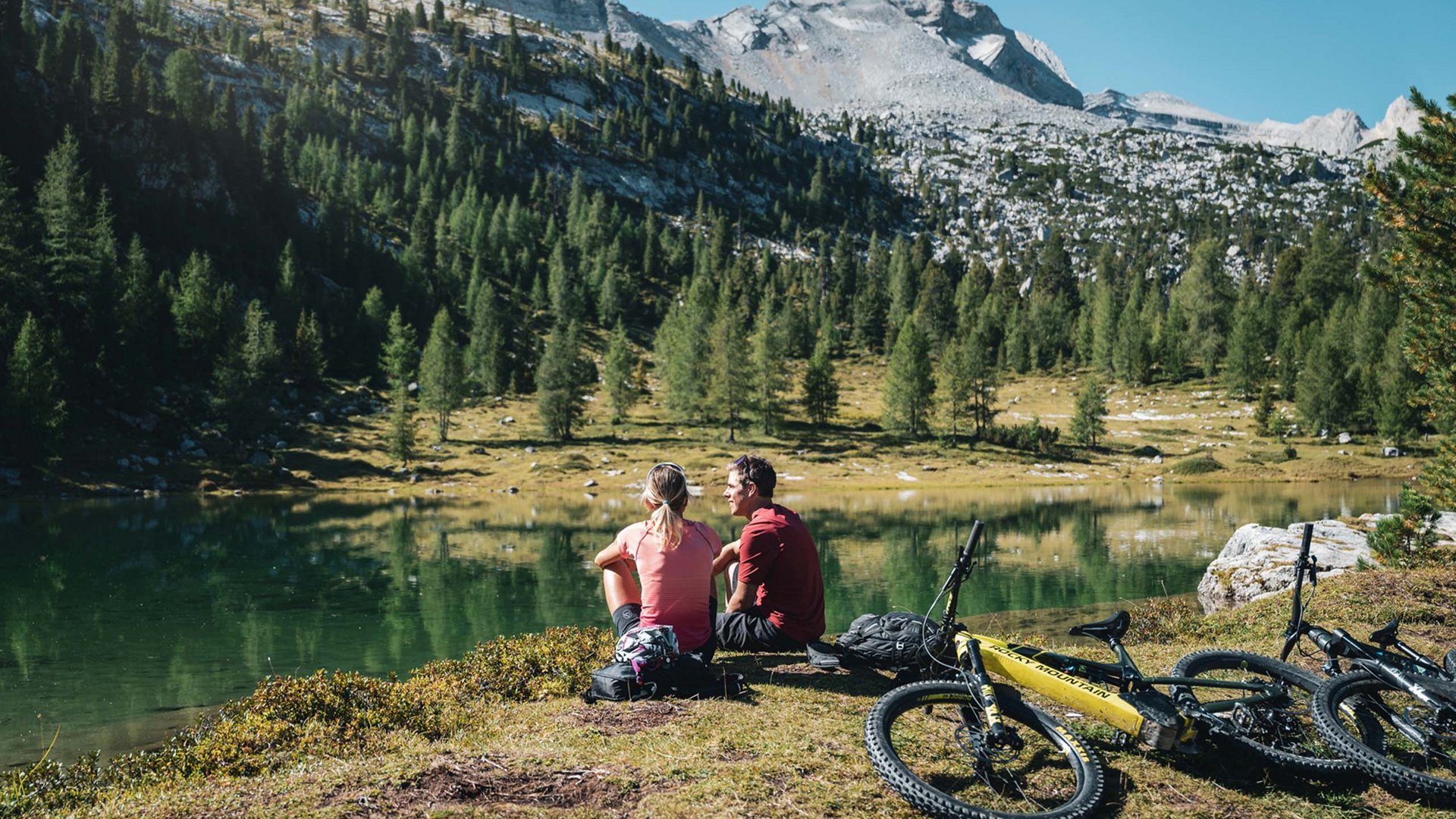 Bike-Verleih Zwei Radfahrer sitzen am Seeufer in den Bergen mit Mountainbikes neben sich