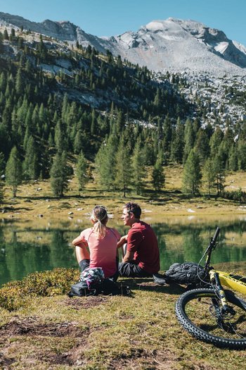 Bike offers and impressions Two cyclists sitting by a mountain lake with mountain bikes beside them