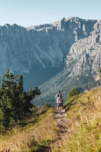 Excelsior: Wanderhotel in den Dolomiten Zwei Wanderer auf einem Bergweg mit Blick auf schroffe Felsen im Hintergrund