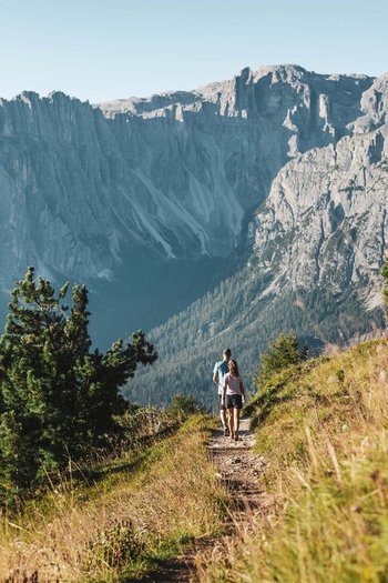 Wanderhotels Südtirol in the Dolomites Two hikers on a mountain trail with rocky cliffs in the background