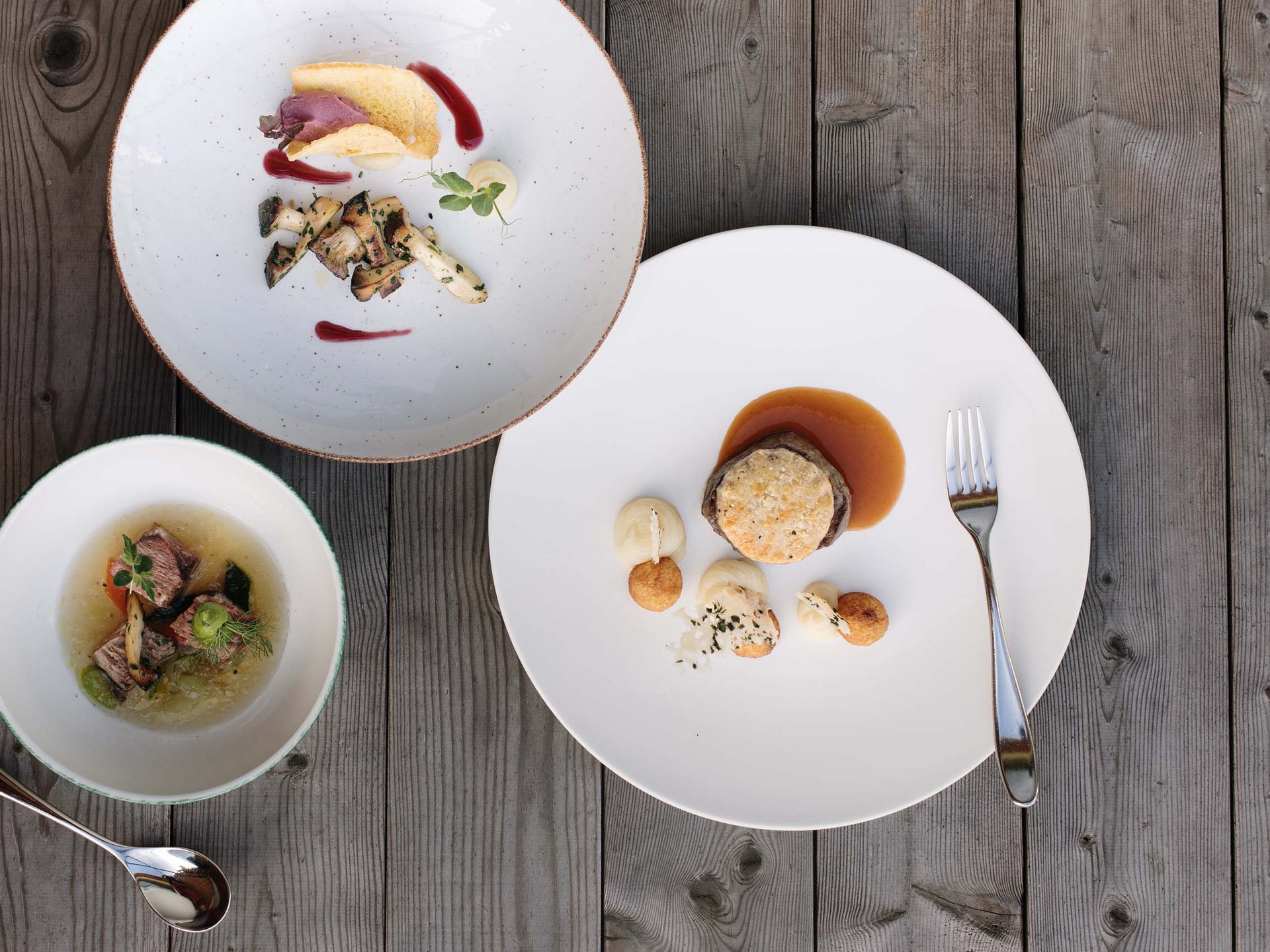 Hotel per celiaci Tre piatti gourmet elegantemente impiattati su tavolo di legno con posate