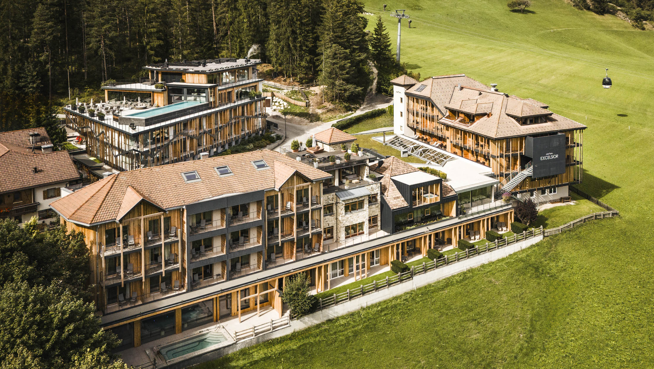 Modern hotel complex with outdoor pool in a green mountain landscape